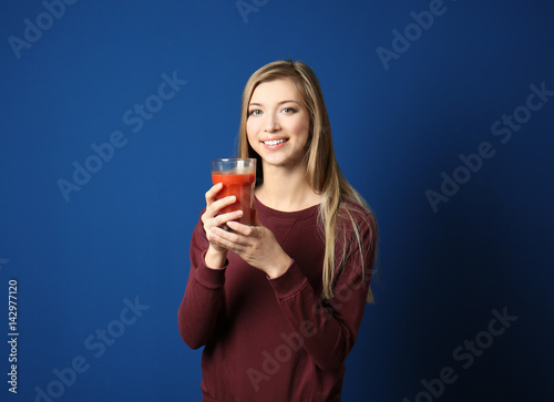Beautiful young woman with glass of fresh juice on dark blue background