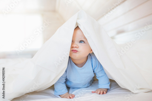 Portrait of funny little baby hides under a blanket