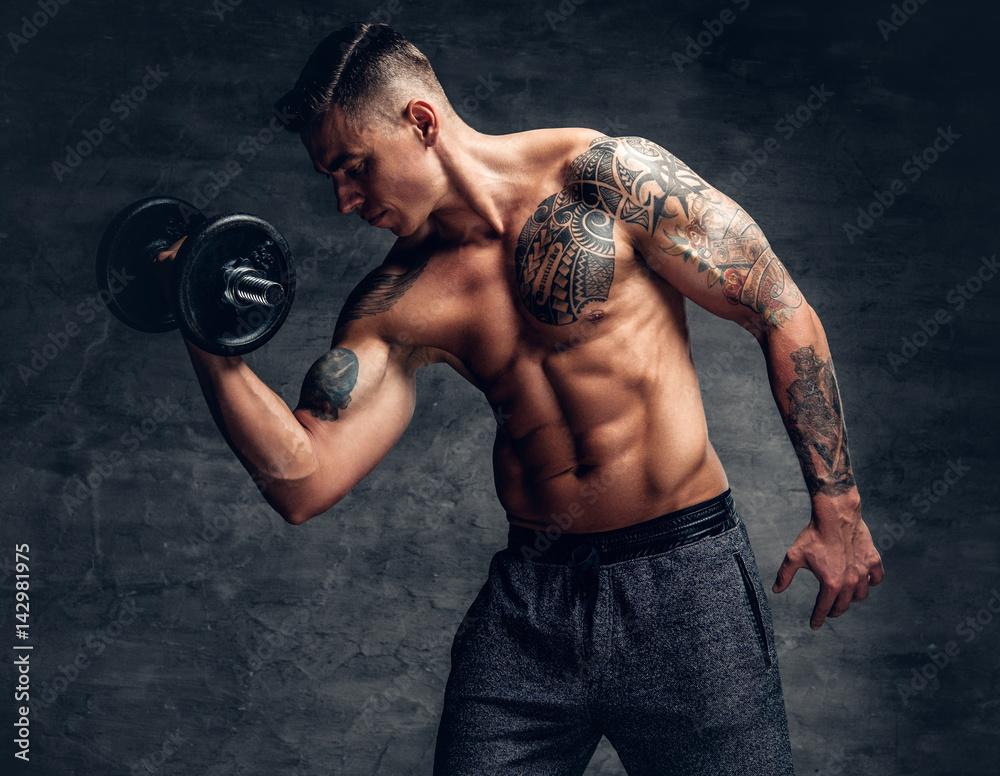 Athletic  male with tattoo on his chest doing biceps workouts with dumbbell.