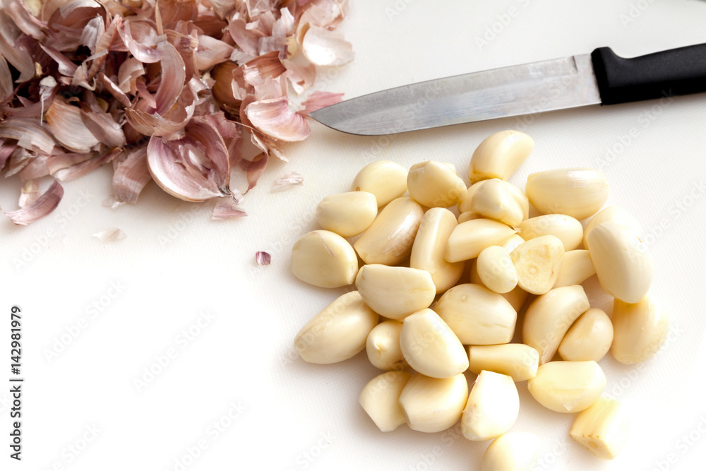 Peeling garlics with knife on white background isolated