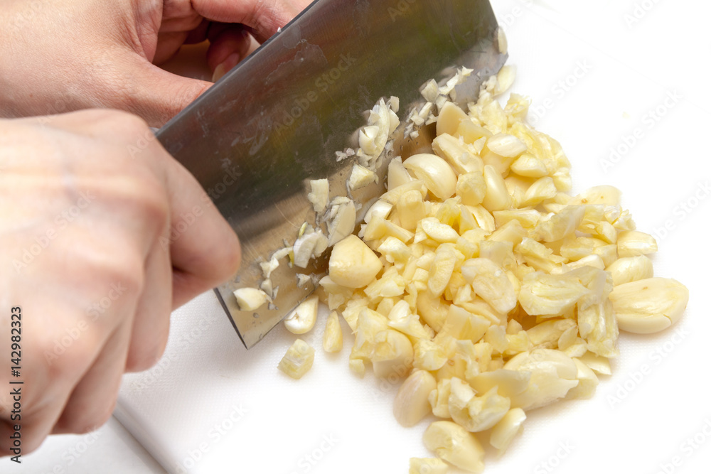 Chopping garlics with knife on white cutting board