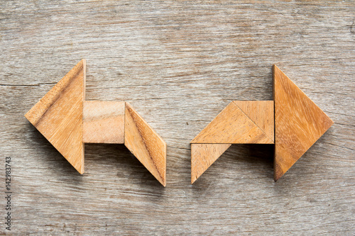 Tangram puzzle as two way arrow shape on wooden background