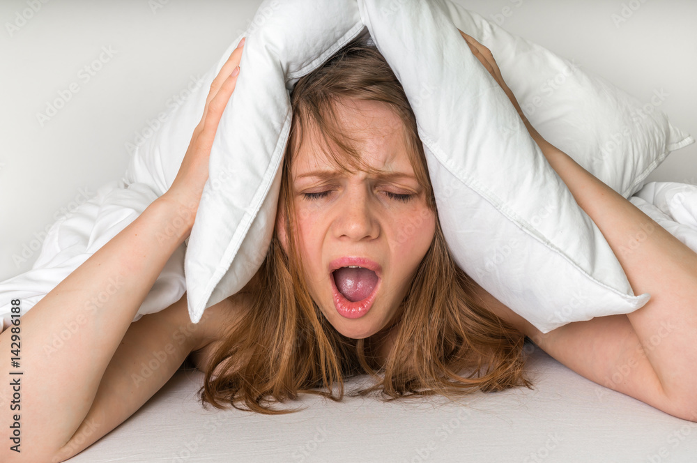 Woman with insomnia covering head and ears with pillow Woman with insomnia covering head and ears with pillow