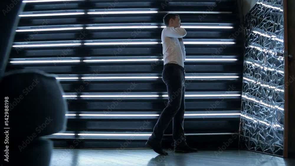Handsome brown-haired man corrects shirt in studio indoors. Attentive male in classic style prepares fashionable clothes, looking in reflection of broken mirror in room with creative design. Preparing