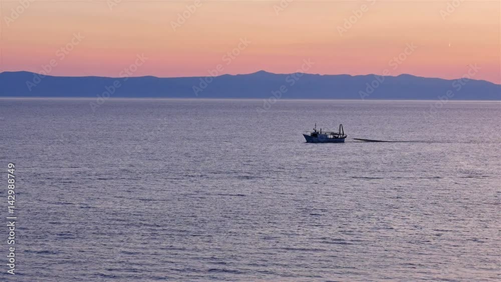 Fishing boat towing net on calm blue Adriatic sea at sunset Fishing boat towing net on calm blue Adriatic sea at sunset