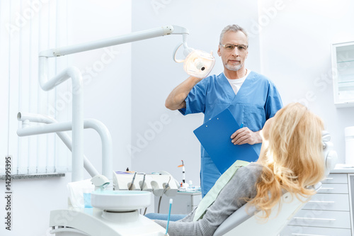 senior dentist in uniform talking with patient in dental clinic