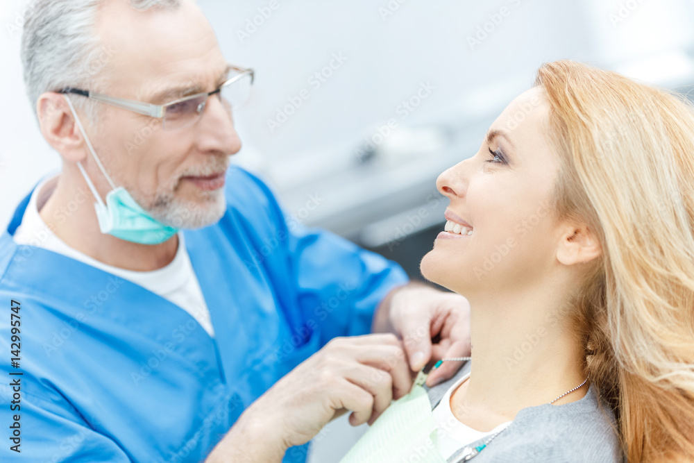 Fototapeta premium senior dentist in uniform talking with patient in dental clinic