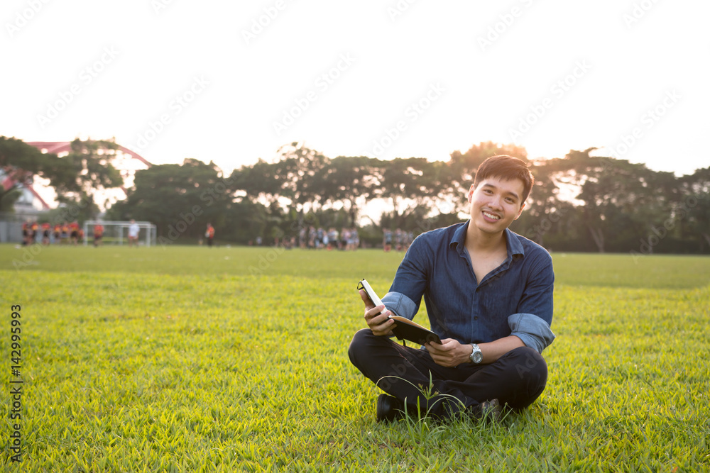 Young asian student men reading a book on greenfiled under sunlight in university Young asian student men reading a book on greenfiled under sunlight in university