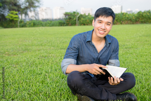 Young asian student men reading a book on greenfiled under sunlight in university © Olly