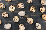 Scattered raw quail eggs on dark wooden background, top view