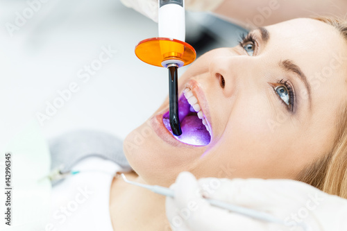 Fototapeta Close-up partial view of dentist using dental curing UV lamp on teeth of patient