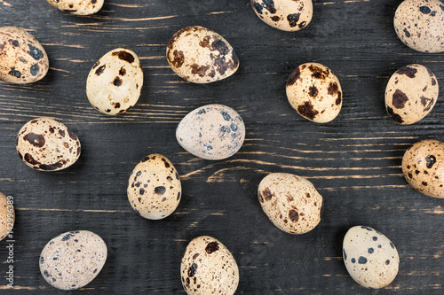 Scattered raw quail eggs on dark wooden background, top view