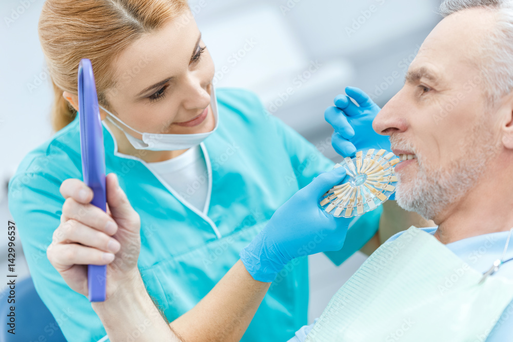Professional dentist with samples comparing teeth of mature patient looking at mirror Professional dentist with samples comparing teeth of mature patient looking at mirror