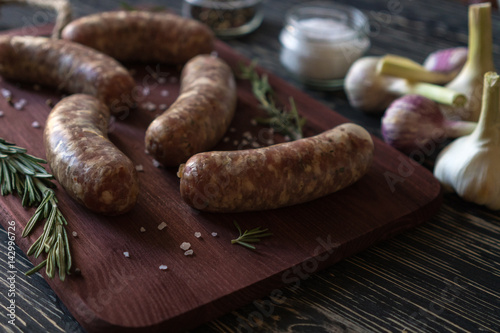 Raw sausages with garlic, rosemary on wooden surface