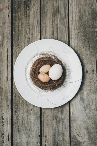 Top view of Easter eggs in nest on white plate on wooden table, Happy Easter concept