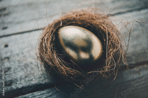 Принти на полотні Close-up view of golden Easter egg in nest on wooden table, Happy Easter concept