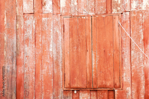 Red painted wood of old traditional wooden thai house with closed window, red background, closeup and detail of weathered wood 