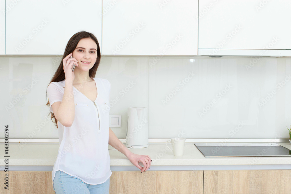 Brunette housewife in white in the kitchen talking on the mobile phone