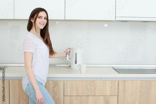 Pretty girl pours water from the kettle in the kitchen