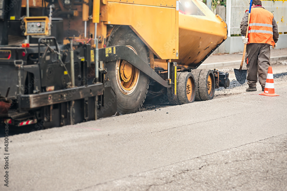 Worker with shovel checks the work of asphalt pavement machine. Worker with shovel checks the work of asphalt pavement machine.