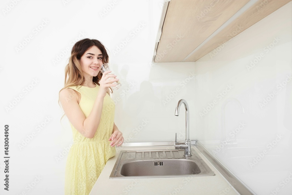 Beautiful young woman holds a glass with water on kitchen Beautiful young woman holds a glass with water on kitchen