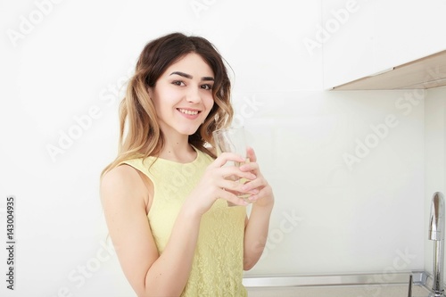 Beautiful young woman holds a glass with water on kitchen