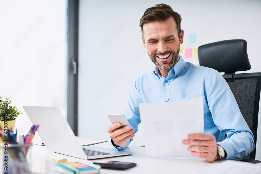 Businessman working at office compare document with his smartphone Businessman working at office compare document with his smartphone