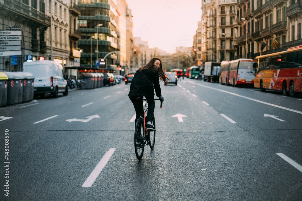 Young tall female cyclist commuting home during a warm sunset throught the one way streets dressed in all black hair flowing in the wind
