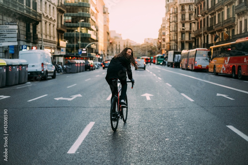 Young tall female cyclist commuting home during a warm sunset throught the one way streets dressed in all black hair flowing in the wind