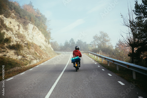 Motorcycle rider goes through the cloudy foggy mist on the top of the mountain road with his little scooter equipped with camping gear and blankets