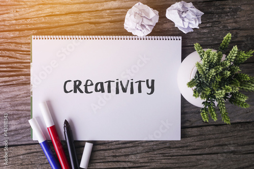 Creativity word with Notepad and green plant on wooden background.