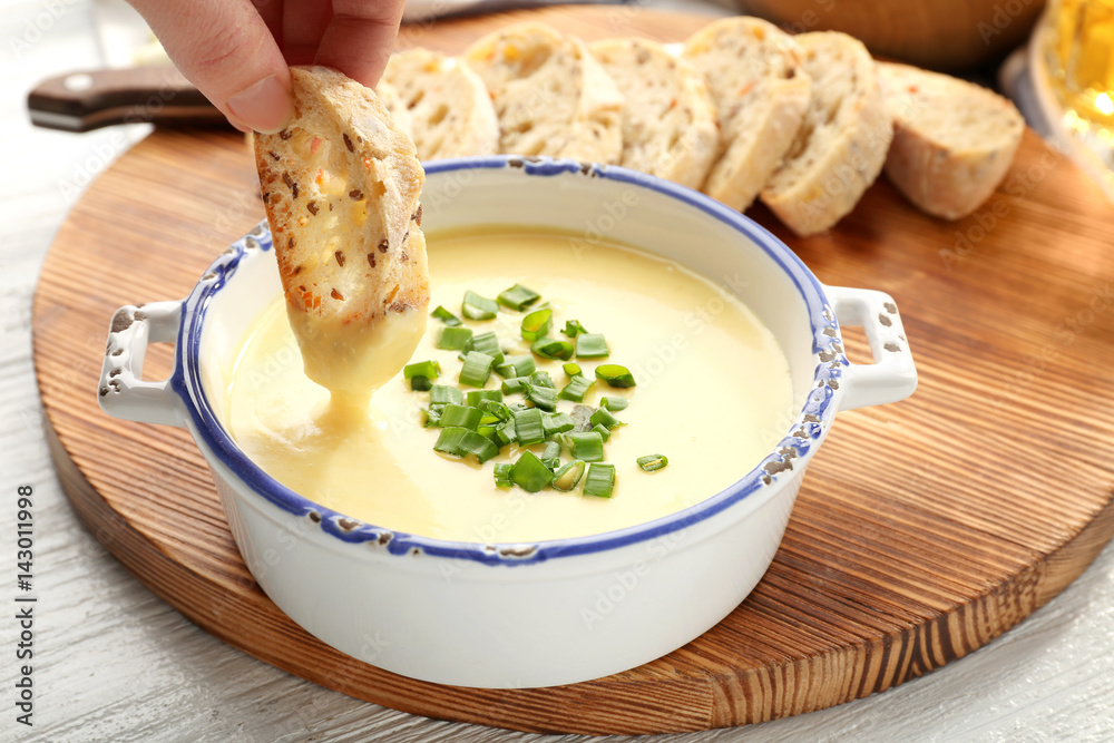 Φωτογραφία Female hand dipping slice of bread in saucepan with beer cheese dip