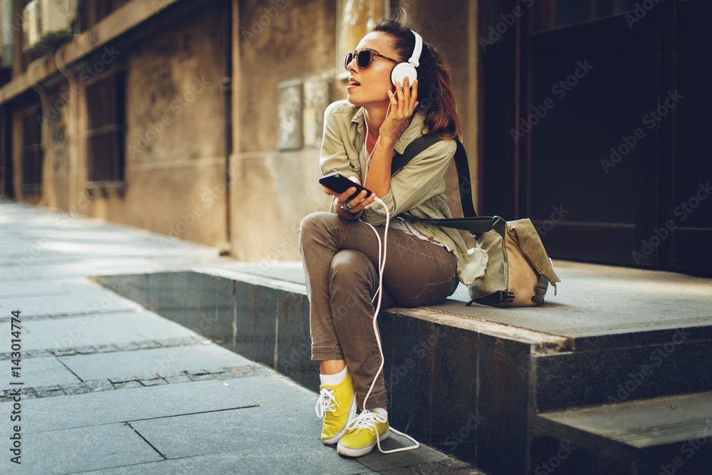 Φωτογραφία Young woman listening to music via headphones on the street