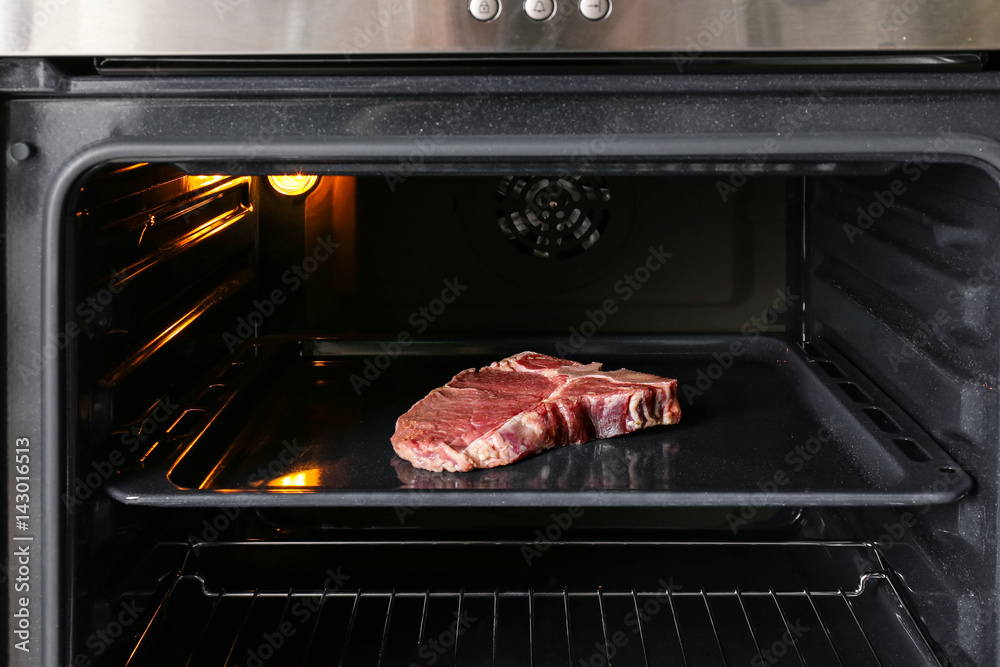 Raw steak on tray in oven Raw steak on tray in oven