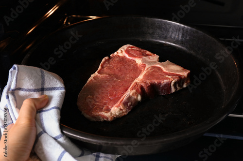Woman putting pan with raw steak into oven