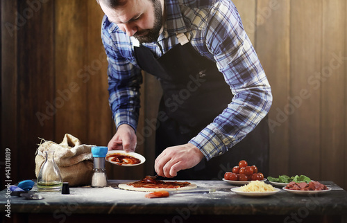 man in an apron preparing a pizza, knead the dough and puts ingr photo