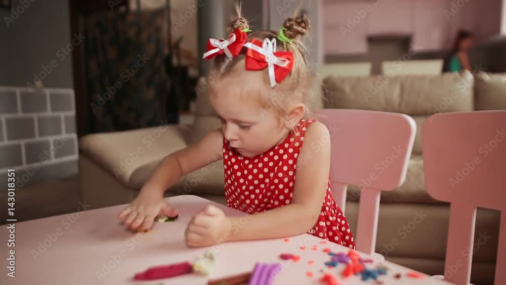 A charming little girl sculpts from plasticine at a table in her room. A charming little girl sculpts from plasticine at a table in her room.