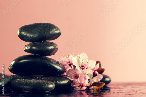 Beautiful pink Spa Flowers on Spa Hot Stones on Water Wet Background. Side Composition. Copy Space. Spa Concept. Pink Background.
