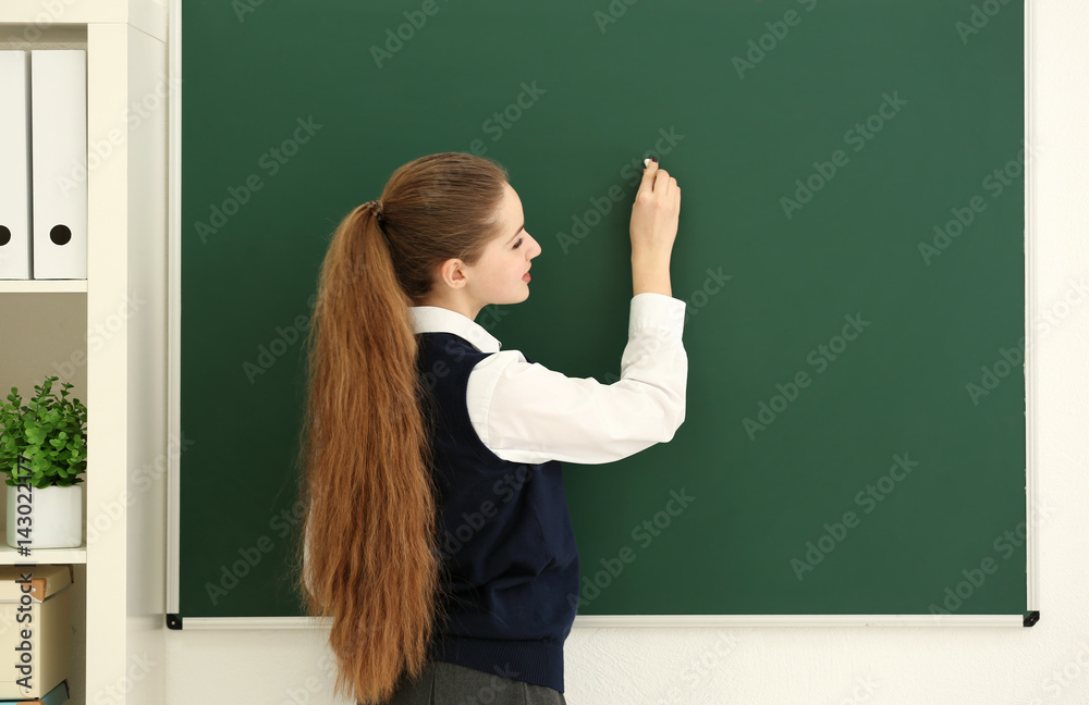 Beautiful long-haired schoolgirl writing at blackboard in classroom Beautiful long-haired schoolgirl writing at blackboard in classroom