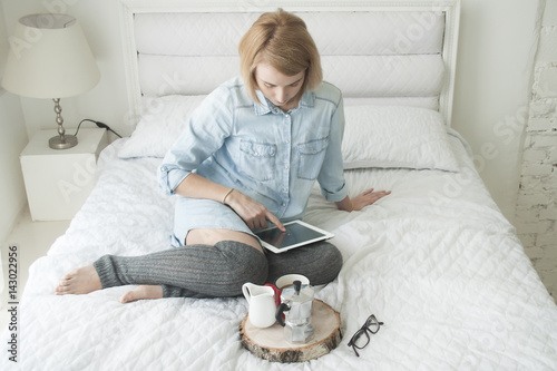 Girl drinking morning coffee on a white bed working on tablet in high stockings photo