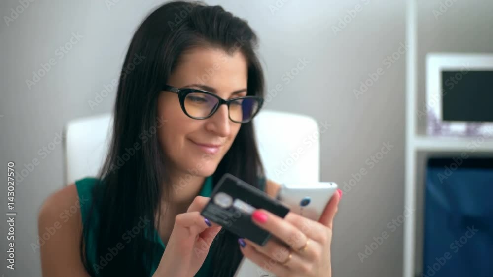 Woman entering data using smartphone while holding a credit card in the other hand Woman entering data using smartphone while holding a credit card in the other hand