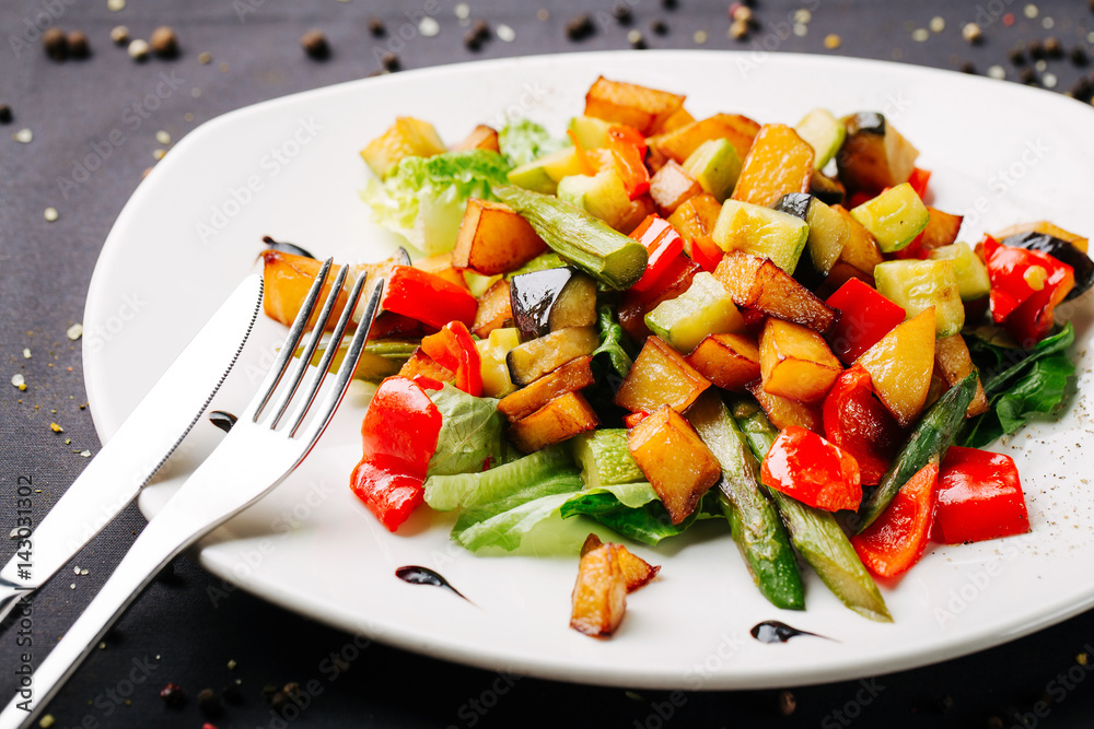 Close up of stir-fried vegetables, potatoes, green beans, pepper on a white plate. Black background is decorated with pepper peas, top view