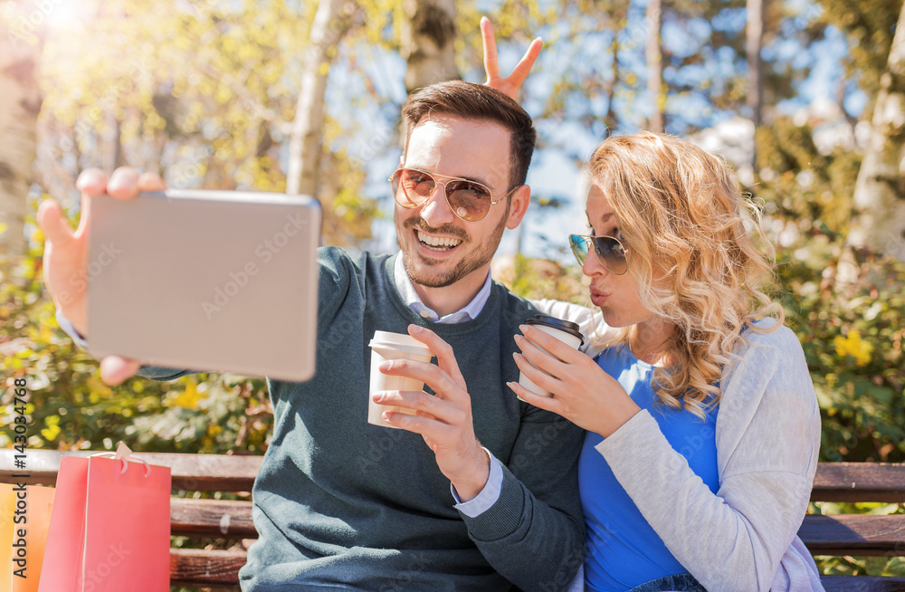 Coffee break after shopping in the spring park. Couple taking a selfie with tablet. Love, relationships, fashion, lifestyle concept