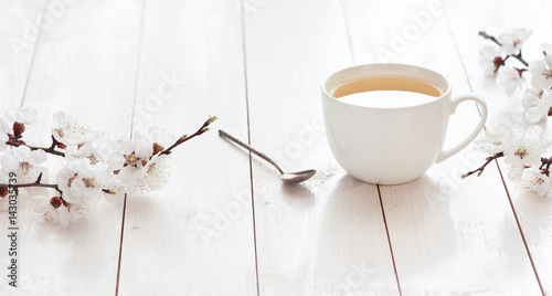 White cup of hot tea with spring flowers on a light wooden background