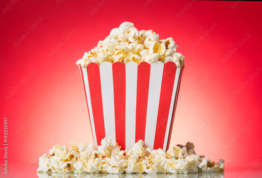 Popcorn in large square box and around on bright red. Popcorn in large square box and around on bright red.