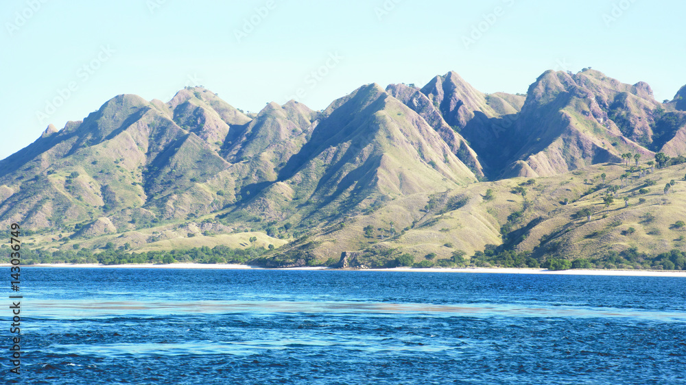 Green vegetation mountain landscape with white beach and blue coastline sea at its foot at Labuan Bajo Bajawa, Indonesia.