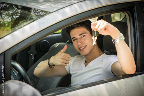 Young handsome male sitting in car and showing big thumb and keys while smiling at camera.  © theartofphoto