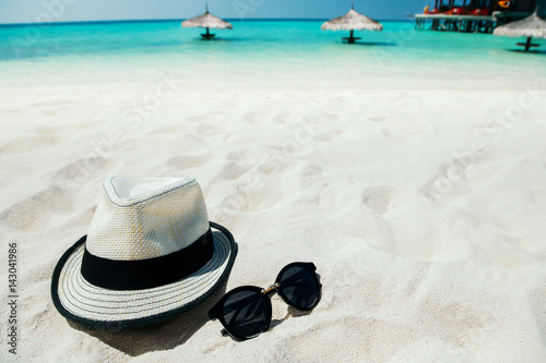 Sunglasses and hat on white sand beach at tropical island