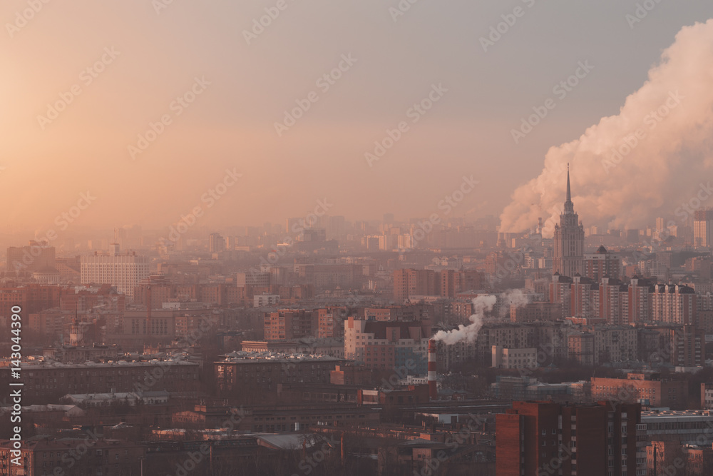 Close-up shooting from high point of metropolitan city: residential buildings illuminated by morning sun, Government building, smoke from fuming chimneys in distance polluting environment