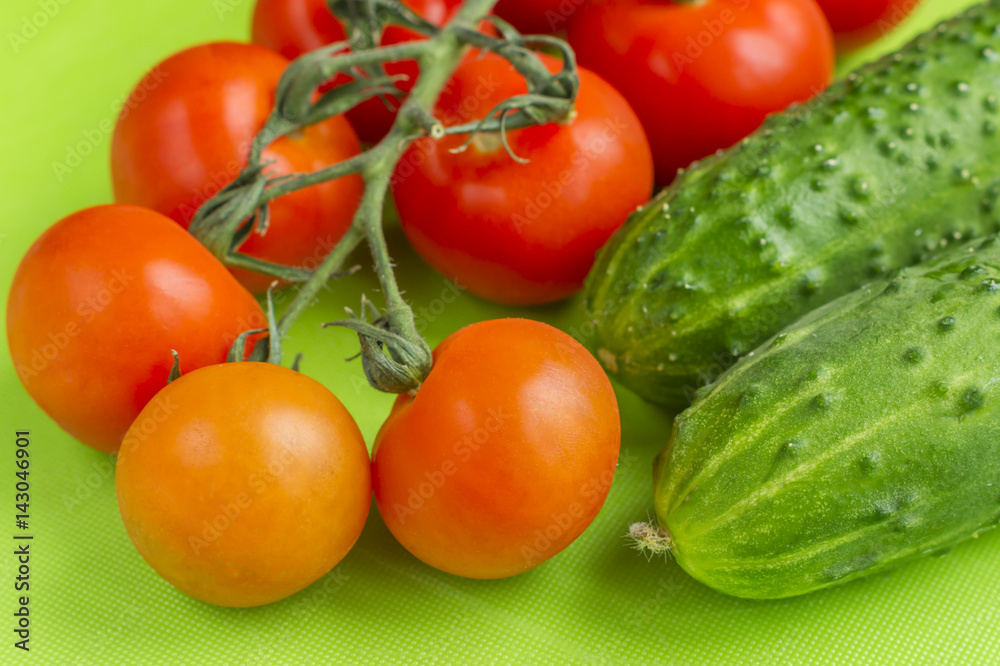 Red cherry tomatoes and green cucumbers on green cutting board. Red cherry tomatoes and green cucumbers on green cutting board.
